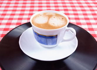Cup of coffee on a vinyl record and red-white vichy tablecloth