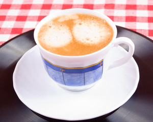 Cup of coffee on a vinyl record and red-white vichy tablecloth