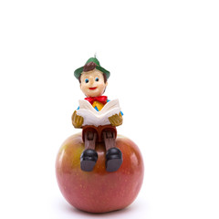 Pinocchio sitting on apple isolated on white background
