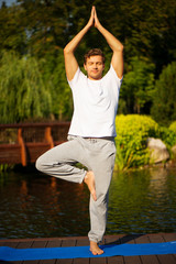 Young man practicing yoga, doing tree pose