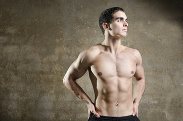 Young fitness man posing on dirty wall background