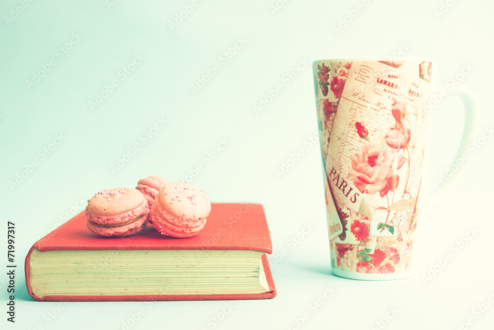 Wall mural Pink macaroons over vintage book and tea cup