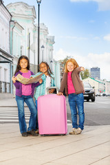 Three smiling girls stand with map and luggage