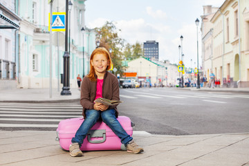 Smiling girl sit on pink luggage with city map