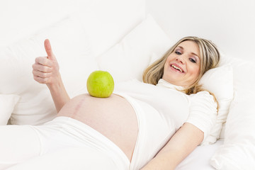 pregnant woman resting in bed with a green apple