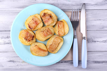 Baked potato with bacon on plate, on wooden background