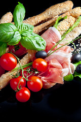 Grissini with prosciutto crudo and vegetables on black