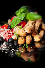 Grissini with prosciutto crudo and vegetables on black