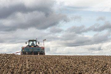 tractor seeding in a field on cloudy sky background