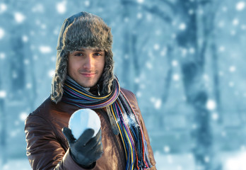 Smiling young man in ear flap hat with a snowball in his hand