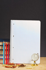 Notebook with colored pencils and globe on a wooden surface.