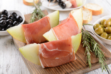 Delicious melon with prosciutto on table close-up