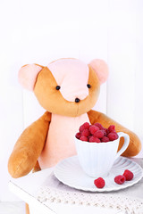 Toy bear and cup of raspberries on wooden wall background