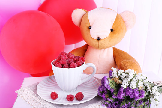 Toy bear, balloons and cup of raspberries