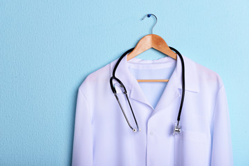 Doctor coat with stethoscope on hanger on blue background