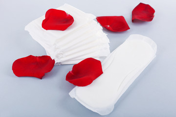 Sanitary pads and rose petals on light background