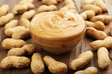 Creamy peanut butter in bowl on wooden table, close-up