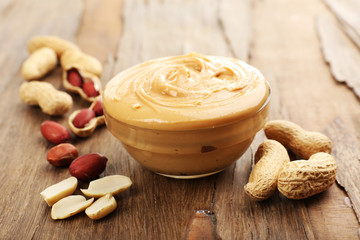 Creamy peanut butter in bowl on wooden table, close-up