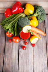 Tomato juice in glass and fresh vegetables on wooden background