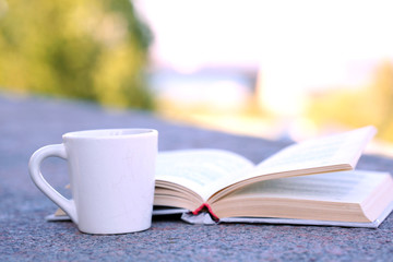 Naklejka premium Cup with hot drink and book, outdoors