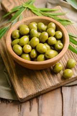 Green olives in bowl with leaves on table close-up