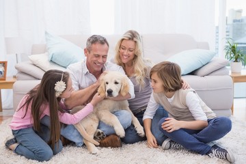 Obraz na płótnie Canvas Smiling family with their pet yellow labrador on the rug