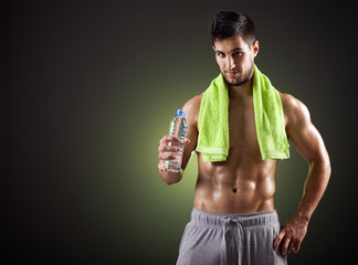 Fitness man holding a bottle of fresh water on dark background