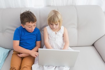 Siblings sitting on the couch using laptop