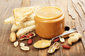 Creamy peanut butter in jar, on wooden table