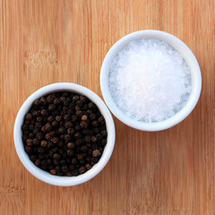 Coarse salt and black peppercorns in white ceramic bowls