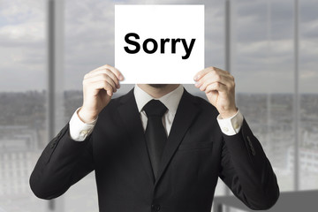 businessman hiding face behind sign sorry