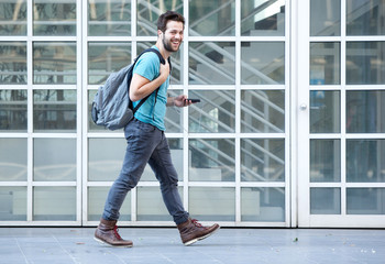 Young man walking on sidewalk with mobile phone and bag