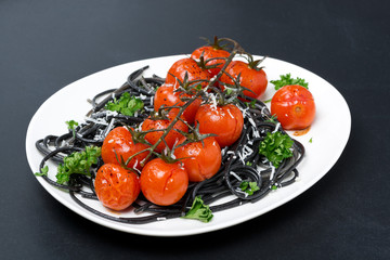 plate of black pasta with baked tomatoes, parmesan cheese