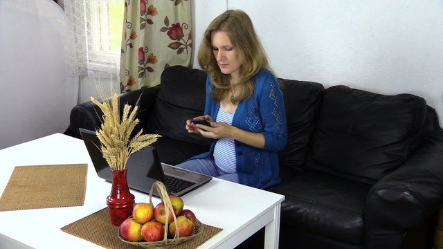 pregnant woman sit at table work with computer and talk on phone