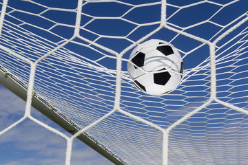 Soccer football in Goal net with sky field.