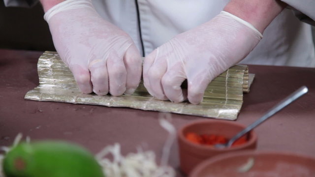 Sushi chef shaping sushi rolls on bamboo mat, cooking process