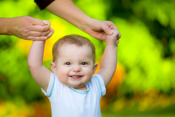 Smiling happy baby learning to walk outdoors