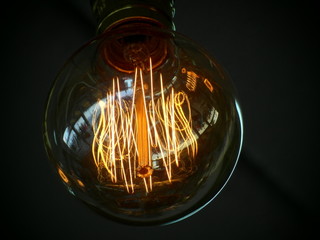 Single edison light bulb with the filaments glowing orange against a dark black background