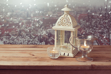 Vintage lantern with candles over winter town background