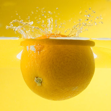 Nice Orange Falling Into Water. Yellow Background.