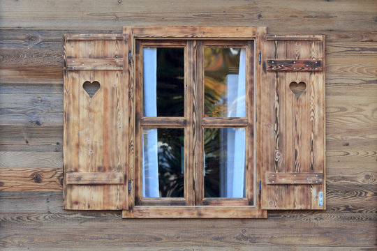 Window of a wooden hut with hearts in the blinds
