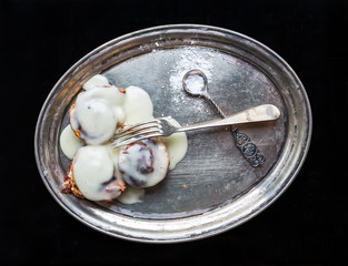 Cinnamon rolls with cream icing and sugar powder on a metal dish
