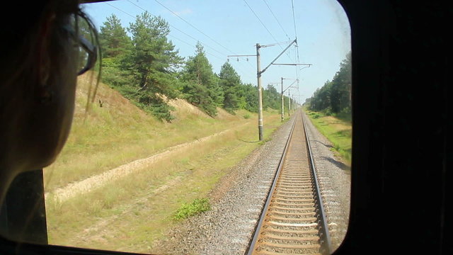 Woman looking through coach window at railway tracks, leaving