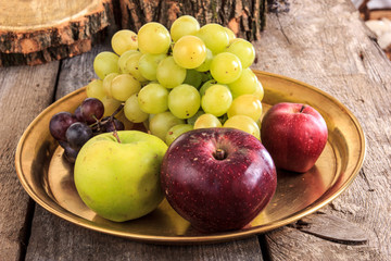 Fresh apples and grapes on golden plate over wooden background