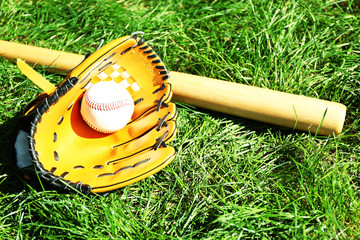 Baseball bat, ball and glove on green grass background