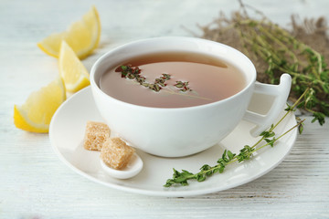 Cup of tasty herbal tea with thyme and lemon, on wooden table