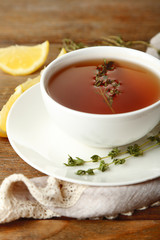 Cup of tasty herbal tea with thyme and lemon on wooden table