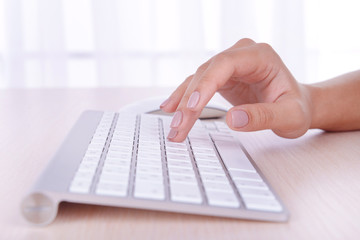 Female hands typing on keyboard on light background