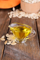 Pumpkin seed oil in glass sauce-boat on wooden background