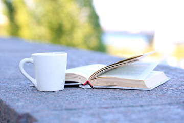 Cup with hot drink and book, outdoors